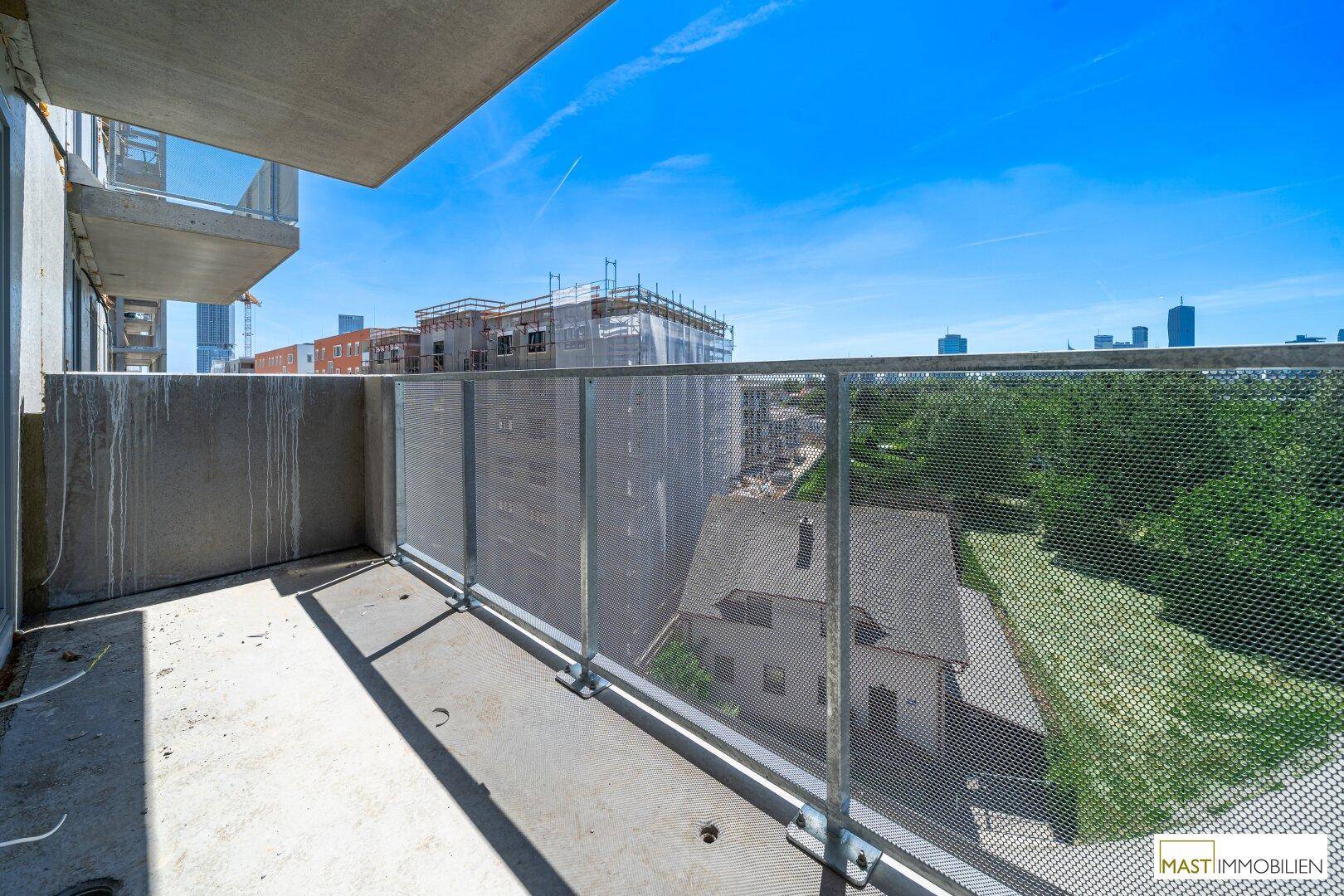 Balkon mit Blick auf umliegende Neubauten und grüne Flächen unter blauem Himmel.