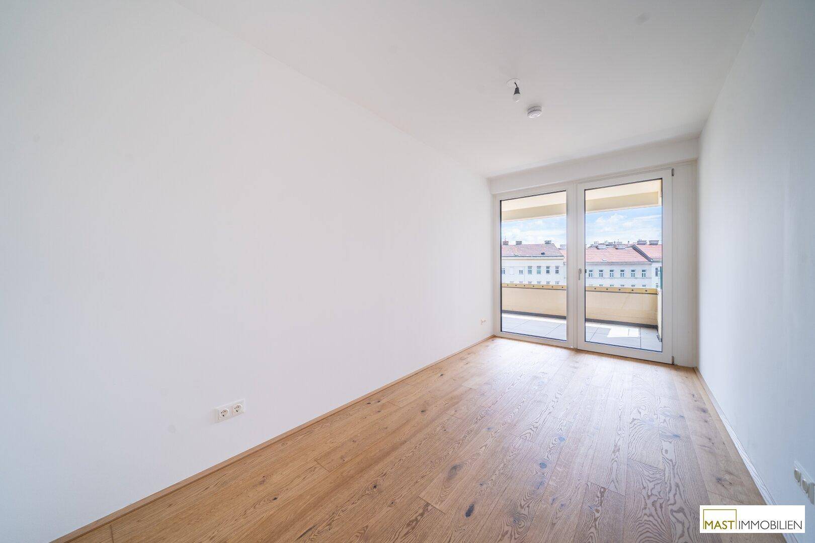 Geräumiges Zimmer mit hellem Parkettboden und großer Glasfront, die viel Tageslicht hereinlässt.