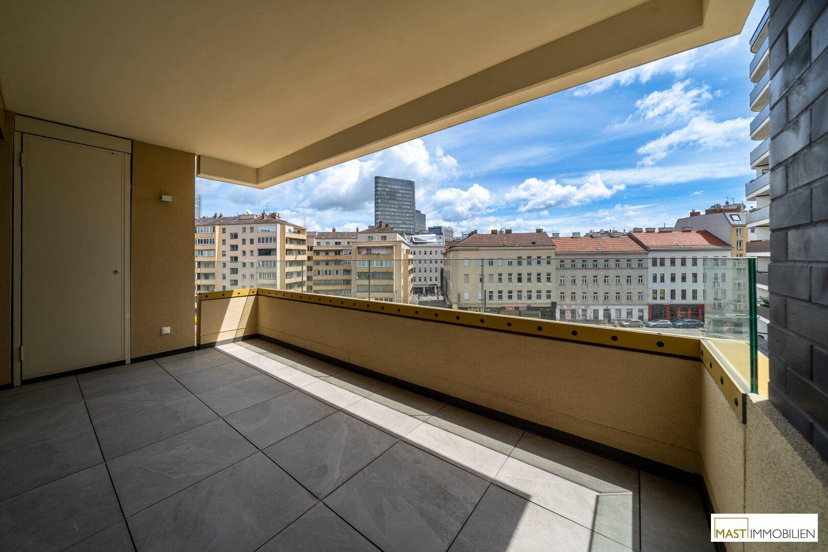 Großer Balkon mit Fliesenboden und Glasgeländer, bietet einen beeindruckenden Panoramablick auf die Stadt.