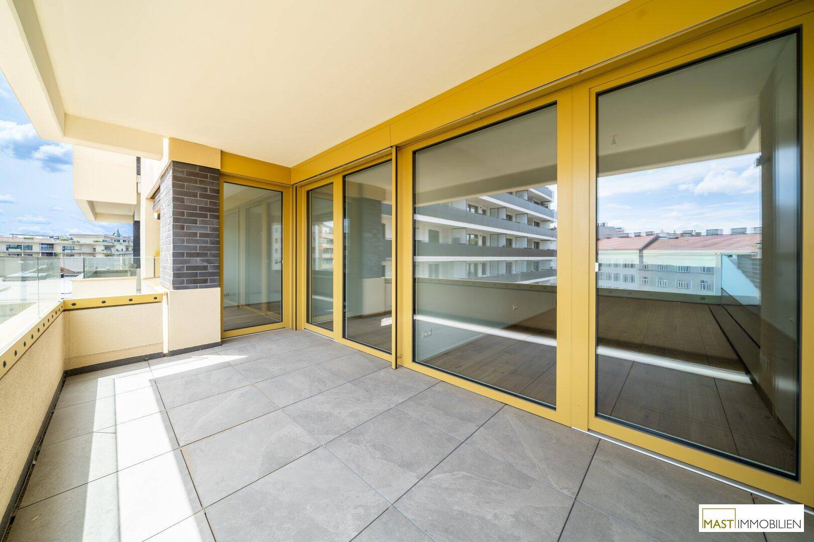 Geräumiger Balkon mit Fliesenboden und gelben Fensterrahmen, bietet einen weiten Blick über die Stadt.