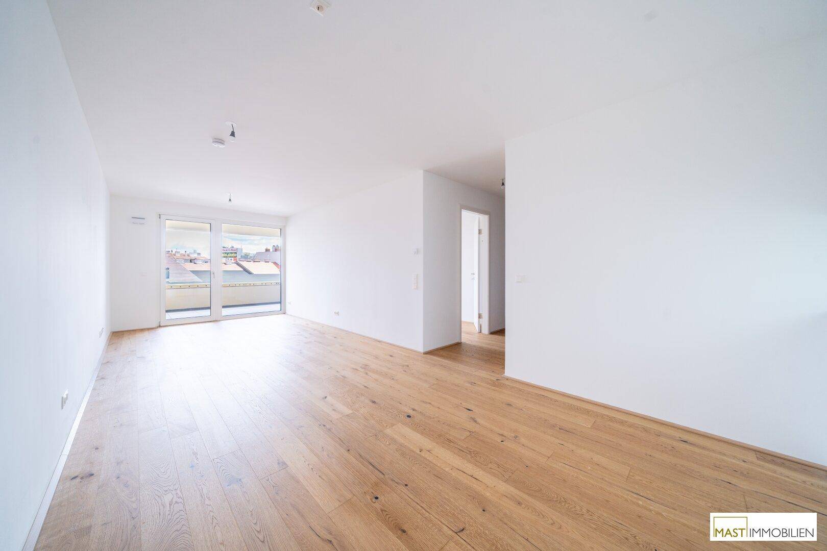 Lichtdurchfluteter Wohnbereich mit Holzparkett und Zugang zu einem Balkon, bietet vielseitige Nutzungsmöglichkeiten.