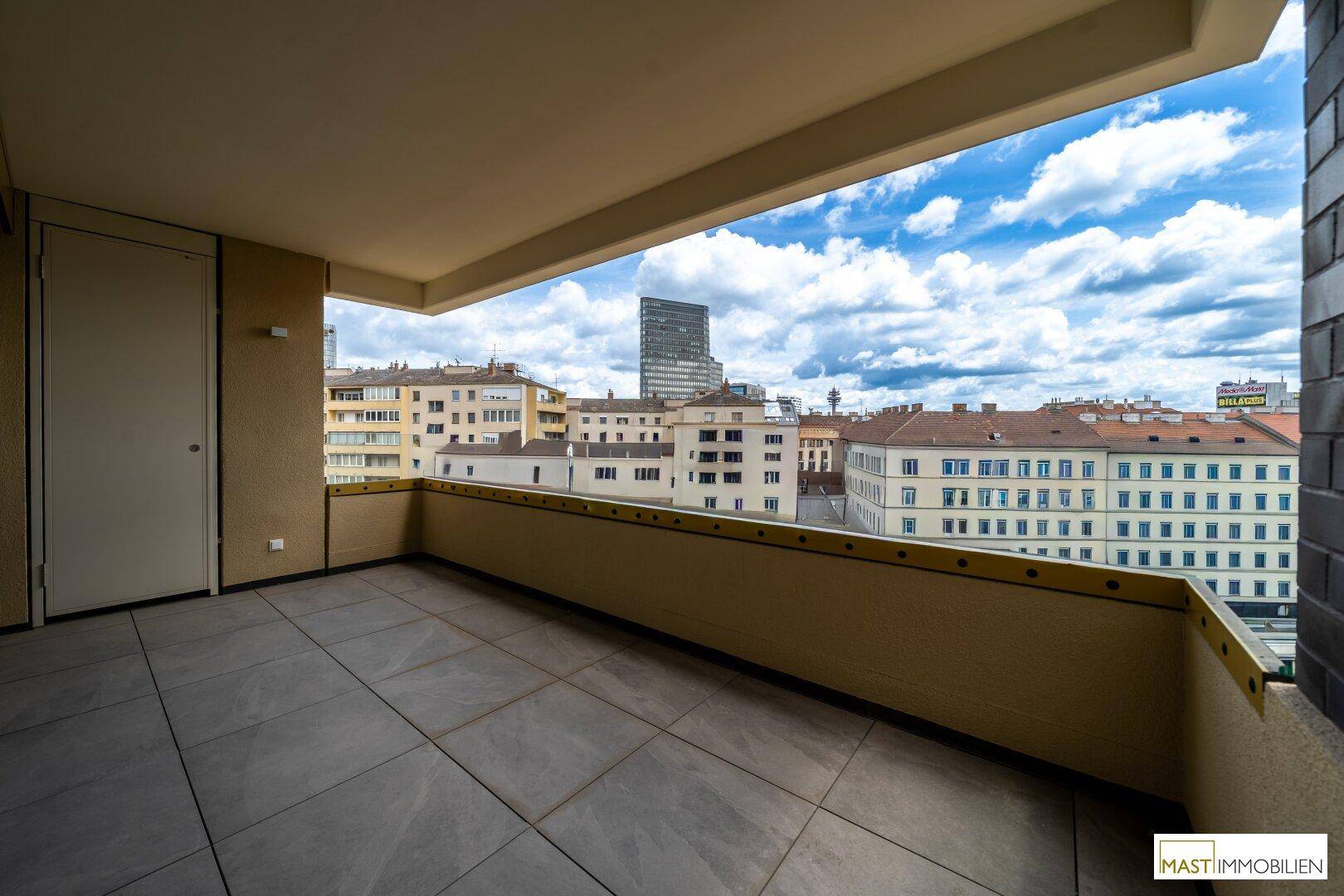 Großer Balkon mit Fliesenboden und weitem Blick über die städtische Skyline und umliegende Gebäude.
