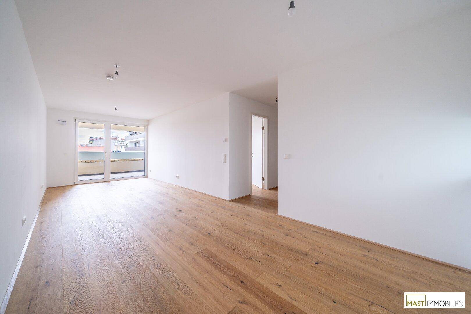 Geräumiges, helles Zimmer mit Holzboden und Zugang zu einem weiteren Raum und Balkon.