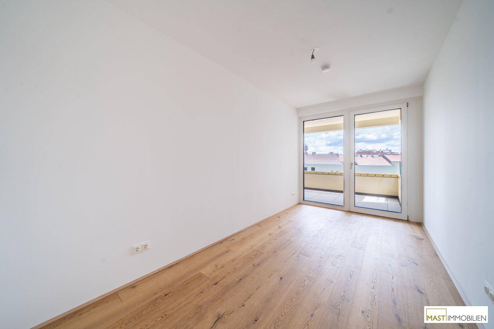 Lichtdurchflutetes Zimmer mit Parkettboden und direktem Zugang zu einem Balkon.