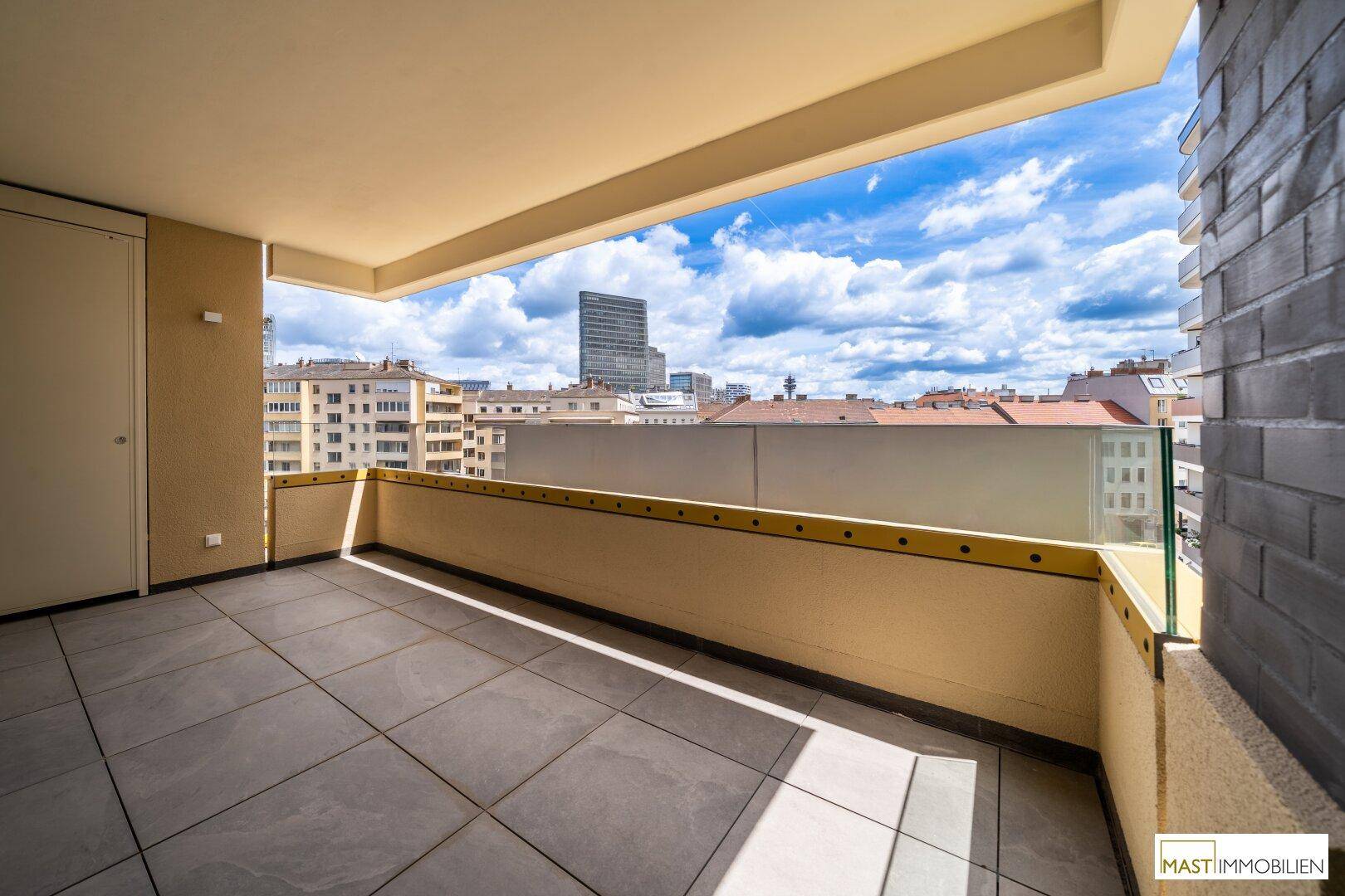 Sonniger Balkon mit Stadtblick und Glasgeländer, ideal zum Entspannen im Freien.