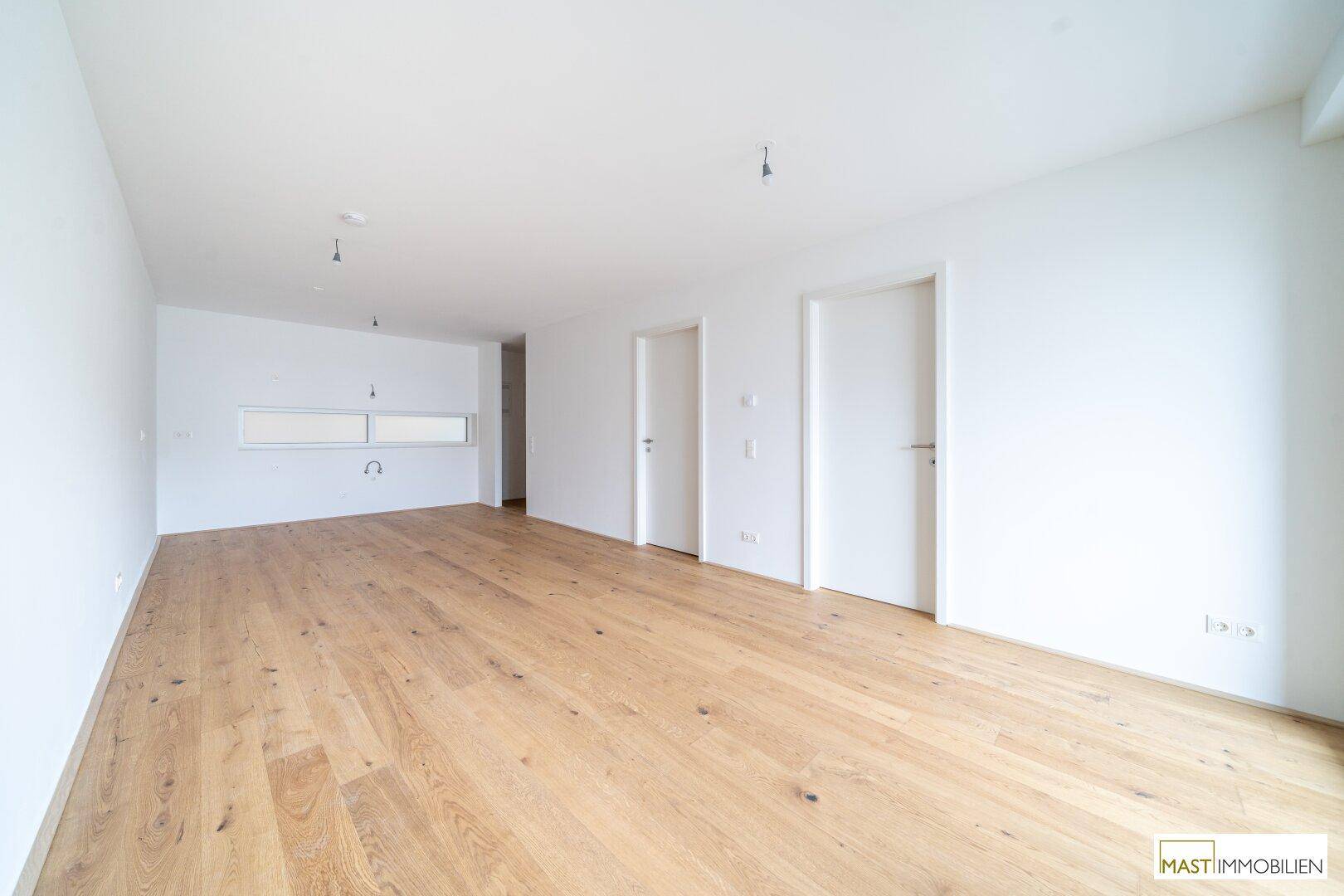 Heller Raum mit Parkettboden und einer Aussparung für eine moderne Einbauküche, ideal für offenes Wohnen.