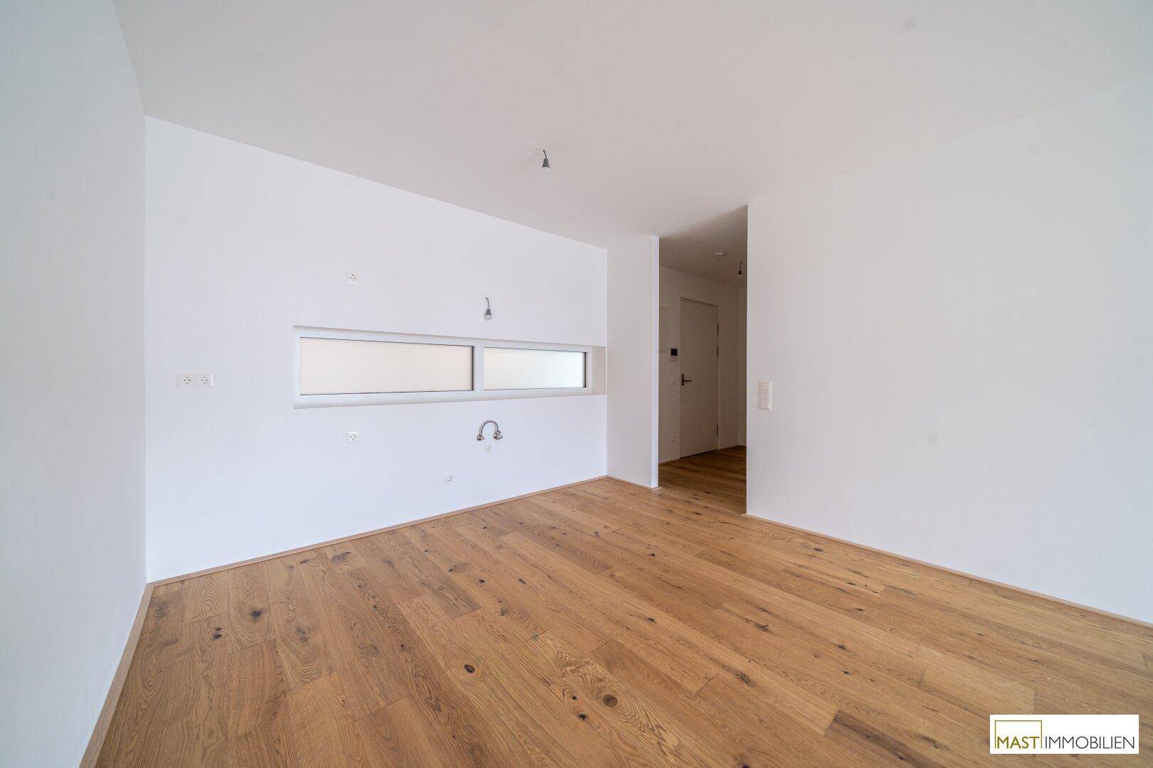 Leerer Küchenbereich mit Parkettboden und einem schmalen Fenster, bereit für die Installation einer modernen Küche.