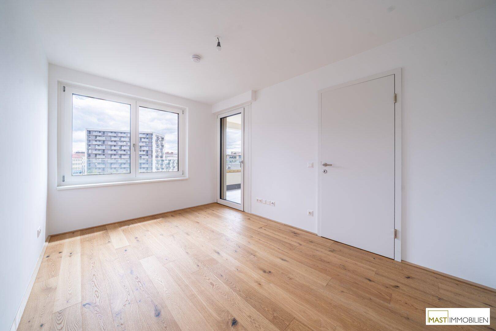 Helles Schlafzimmer mit Parkettboden, großen Fenstern und direktem Zugang zu einem Außenbereich.