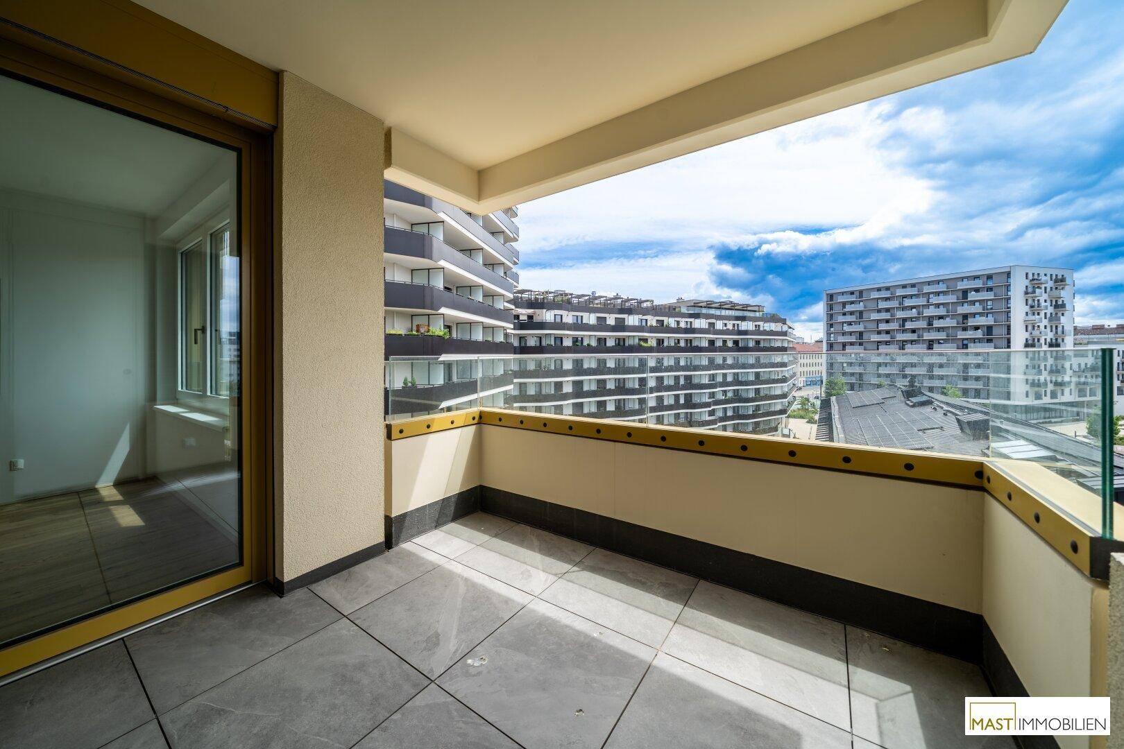 Geräumiger Balkon mit Fliesenboden und Glasbrüstung, bietet einen weiten Blick über die Stadt.