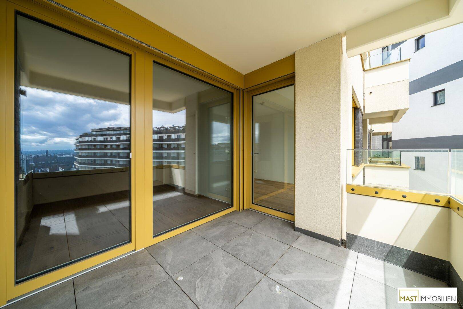 Heller Balkon mit großen Schiebetüren und Fliesenboden, bietet einen Panoramablick auf die Umgebung.