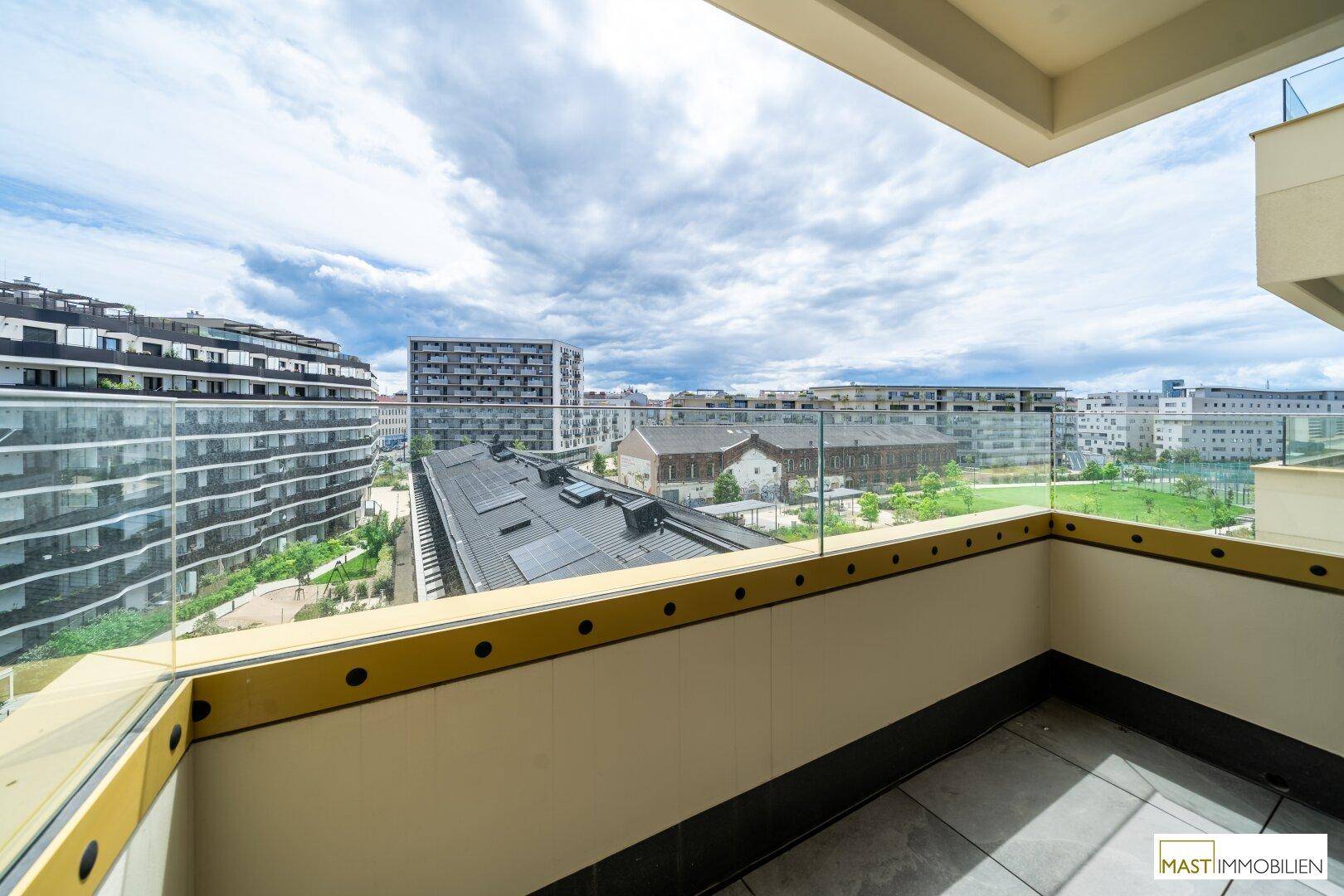 Weitläufiger Balkon mit Glasgeländer und urbanem Ausblick, ideal für entspannte Stunden im Freien.