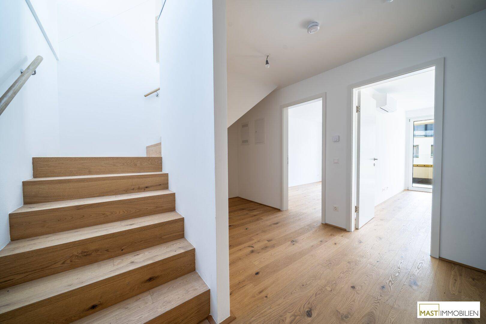 Heller Flur mit Holztreppe, Holzboden und Zugang zu weiteren Zimmern.