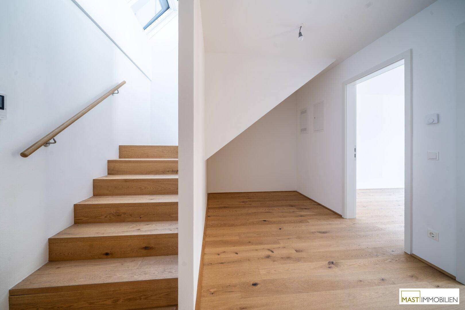 Eingangsbereich mit Holztreppe, Holzboden und weiß gestrichenen Wänden.