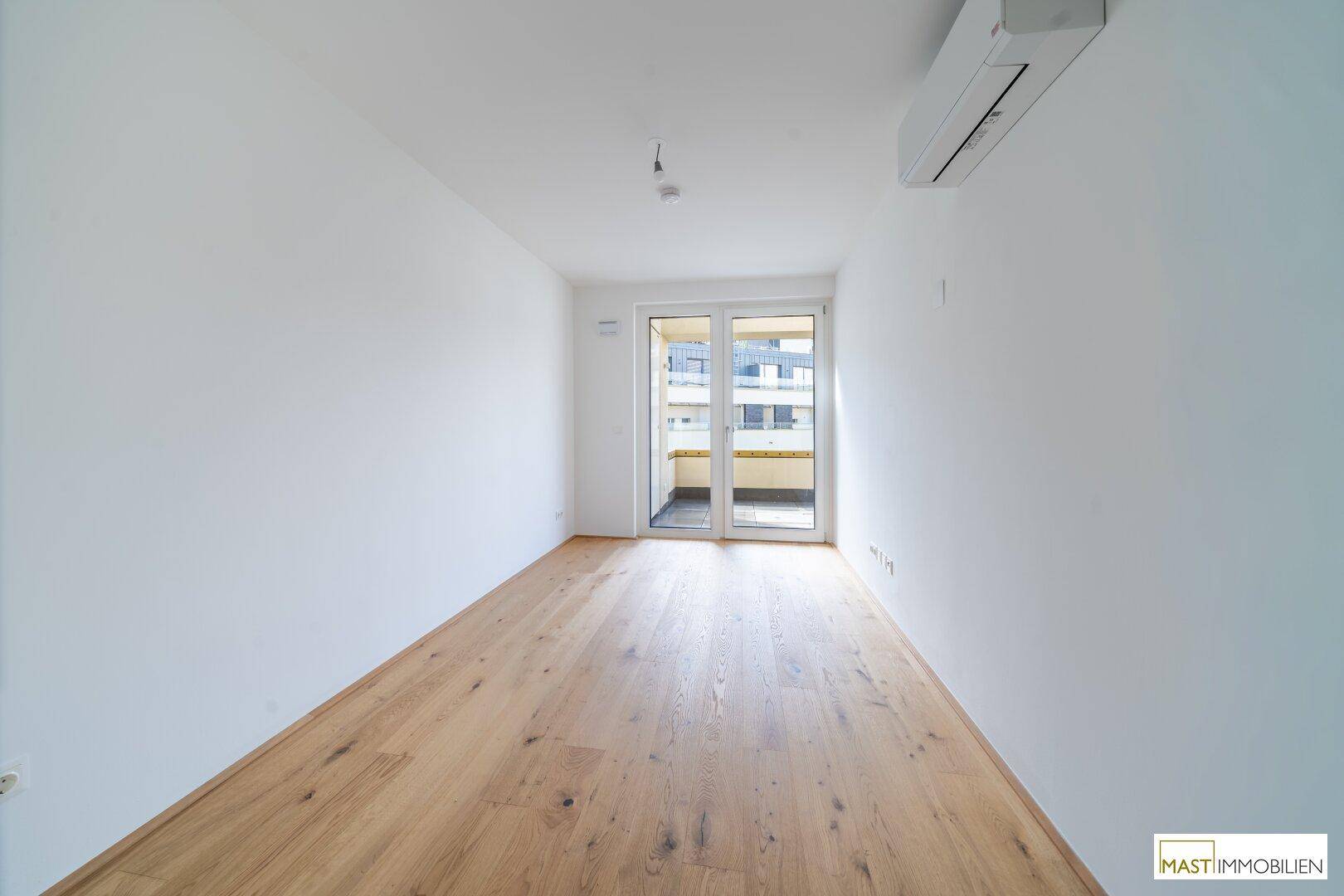 Helles Schlafzimmer mit Holzboden, Klimaanlage und Zugang zu einem Balkon.