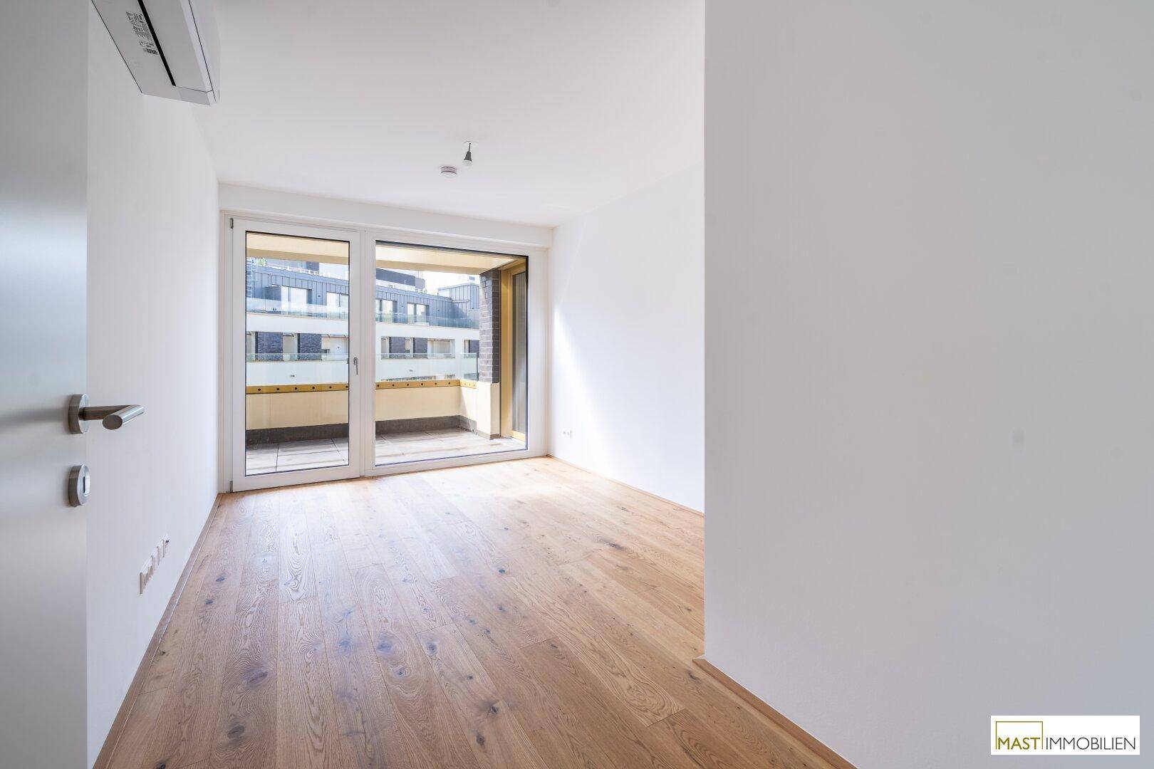 Geräumiges Schlafzimmer mit Holzboden und Balkonzugang, ideal für viel Tageslicht.
