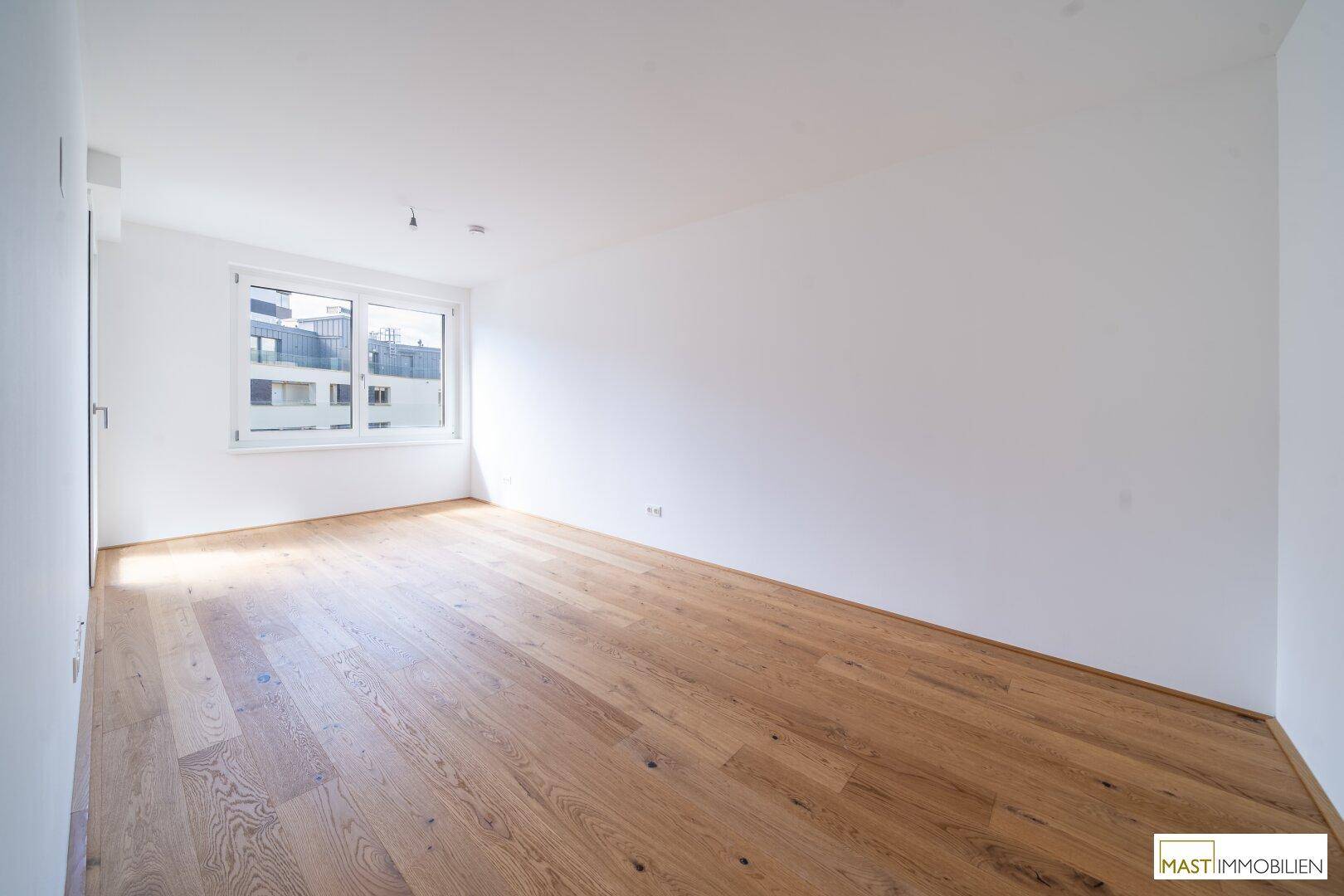 Helles Schlafzimmer mit Holzboden, weißen Wänden und großem Fenster mit Blick nach draußen.