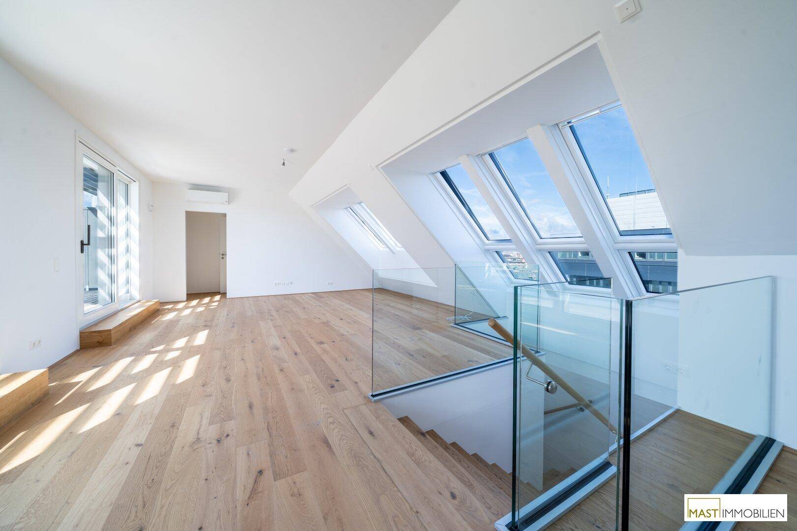 Offener Wohnbereich mit Holzboden, Dachfenstern und moderner Glasbrüstung an der Treppe.