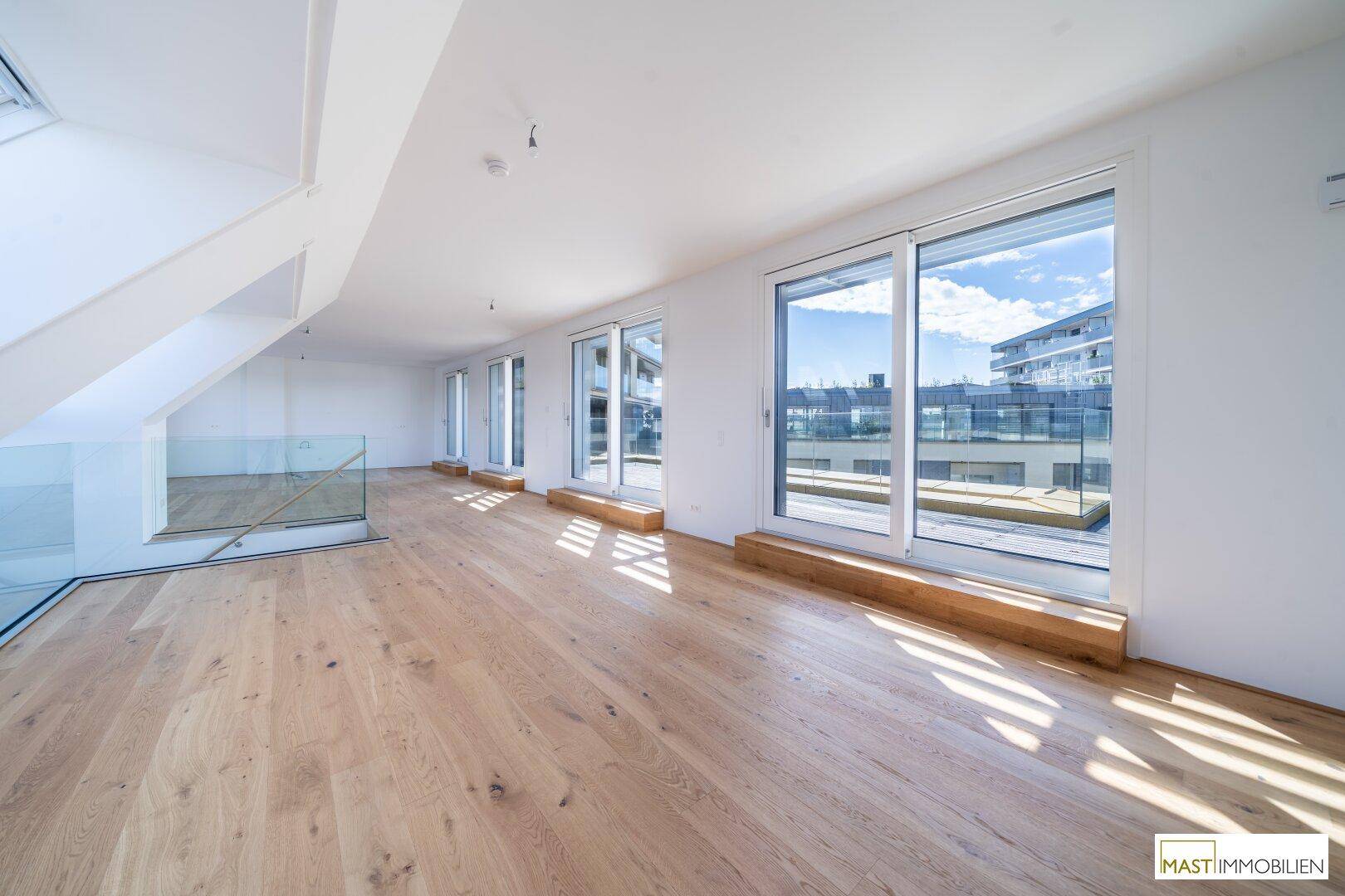 Lichtdurchfluteter Wohnbereich mit Holzboden, bodentiefen Fenstern und Blick auf die Umgebung.