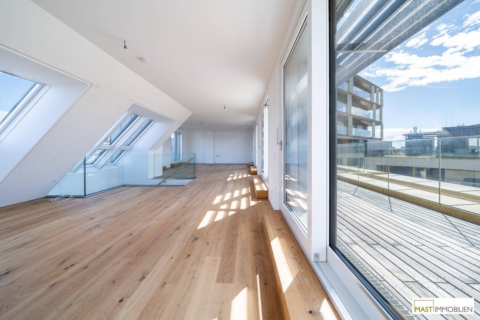 Helles, offenes Wohnzimmer mit Holzboden, großen Fenstern und Zugang zur Dachterrasse.