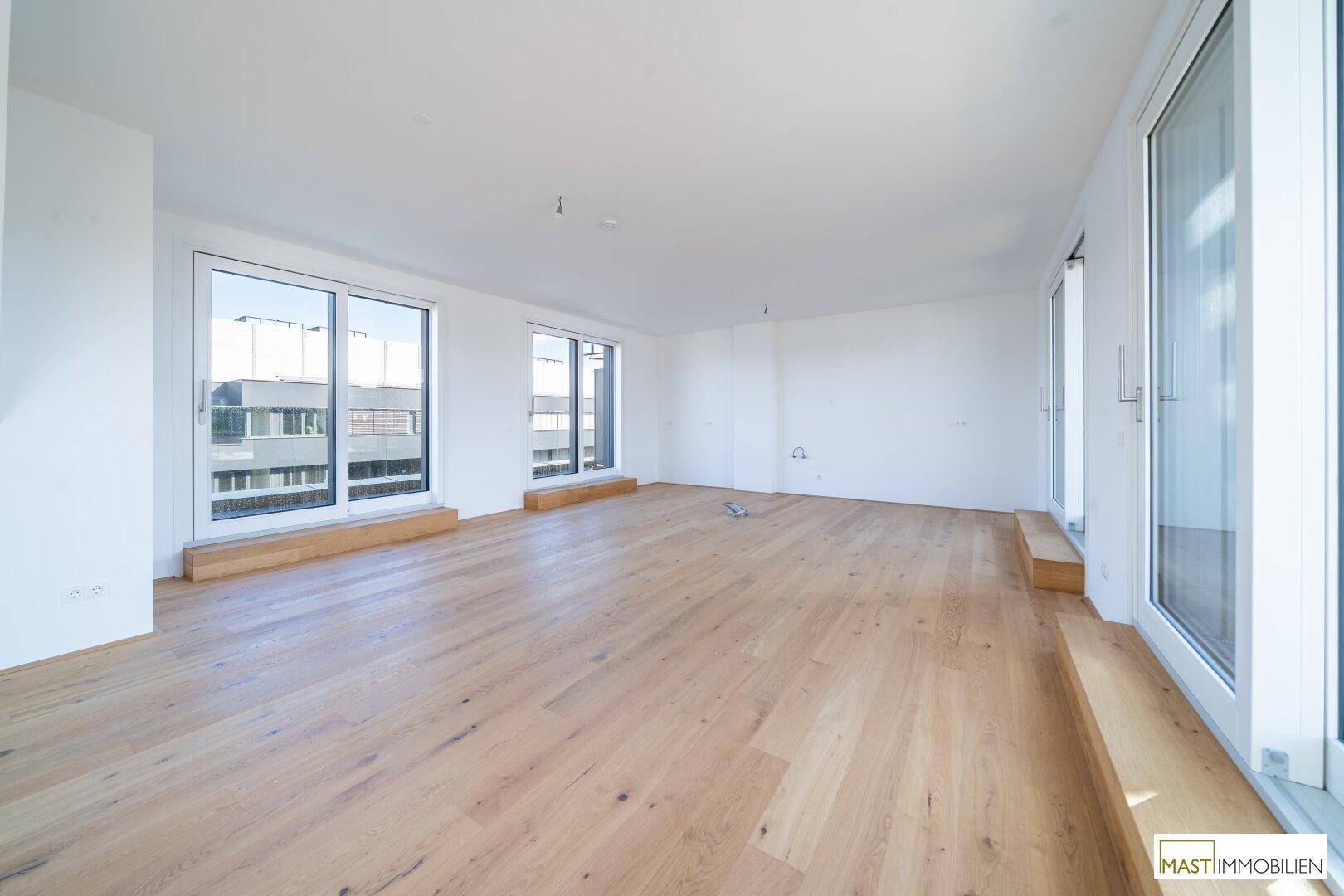 Heller, leerer Wohnraum mit Holzboden und großen Fenstern, die einen weiten Blick bieten.