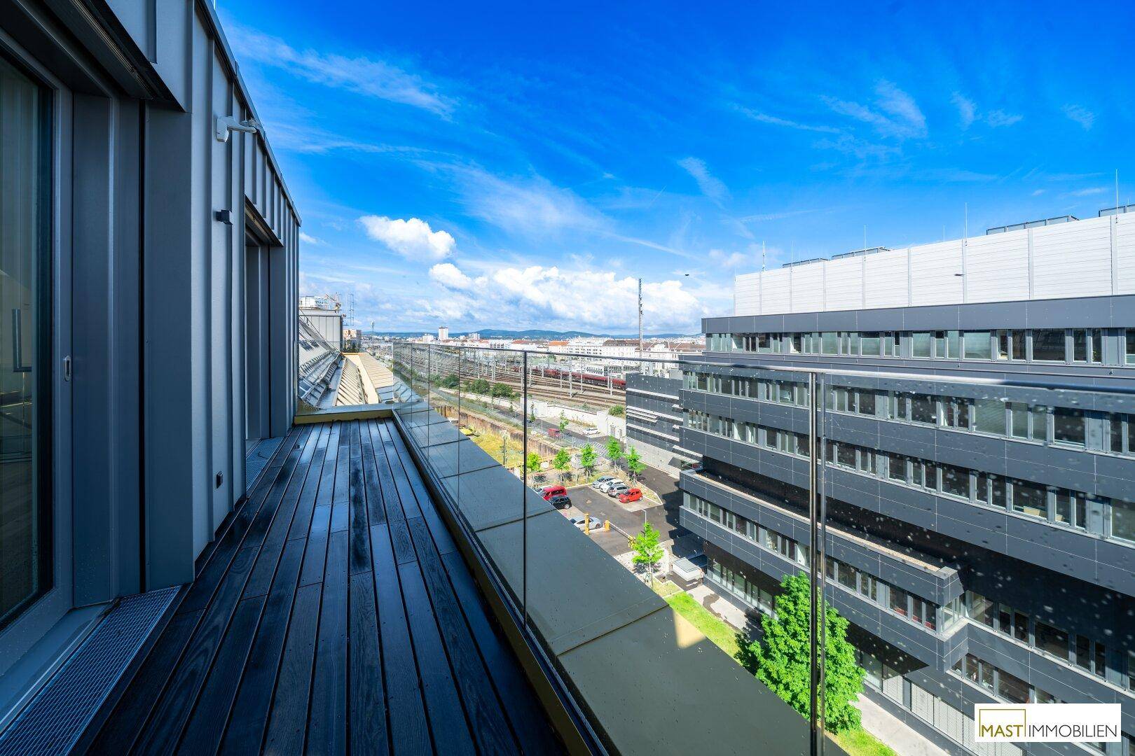 Lange Dachterrasse mit Holzboden, Glasgeländer und Blick auf die Stadt und Bahngleise.