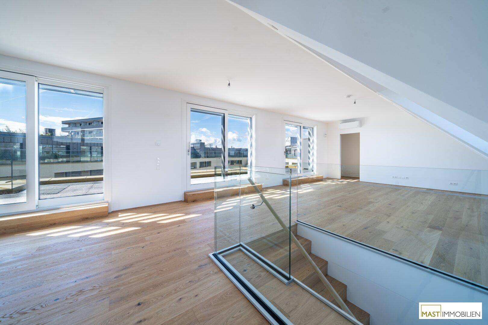Offener Wohnbereich mit Holzboden, Dachfenstern und moderner Glasbrüstung an der Treppe.