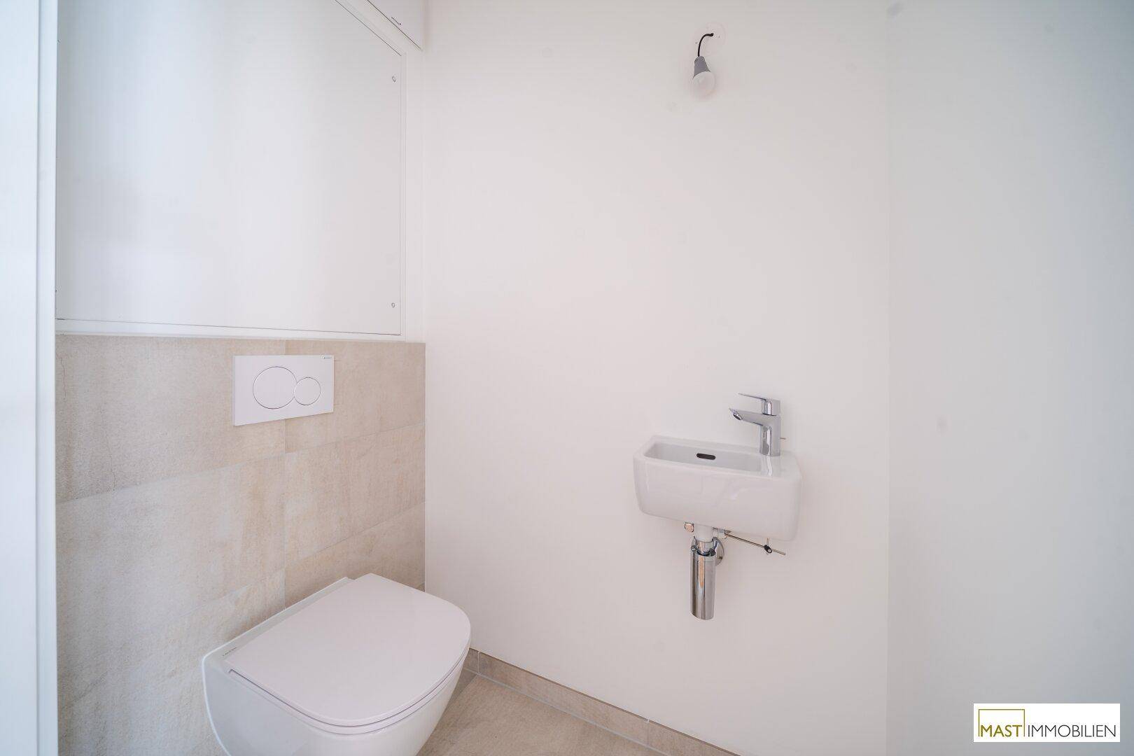 Separates Gäste-WC mit wandhängender Toilette und kleinem Handwaschbecken.