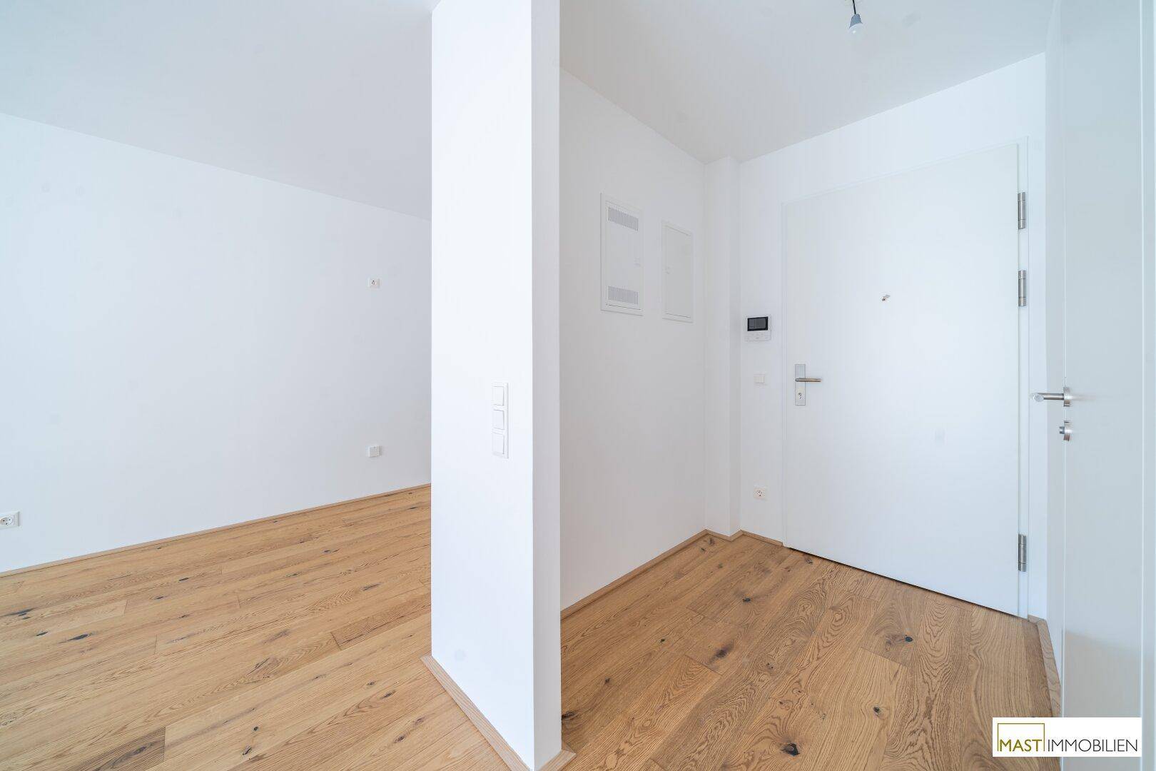 Eingangsbereich mit Holzboden und weißer Tür, der zu den Wohnräumen führt.