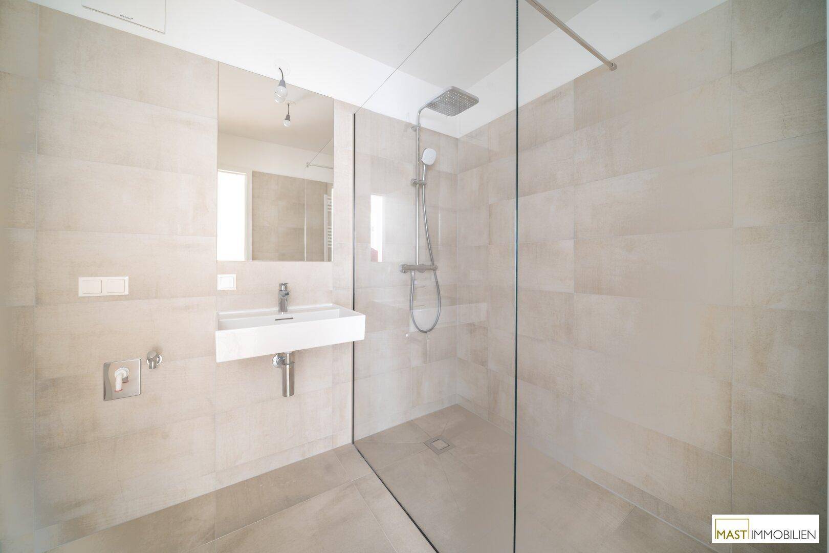 Elegantes Badezimmer mit großer Glasdusche, modernem Waschbecken und hellen Fliesen.