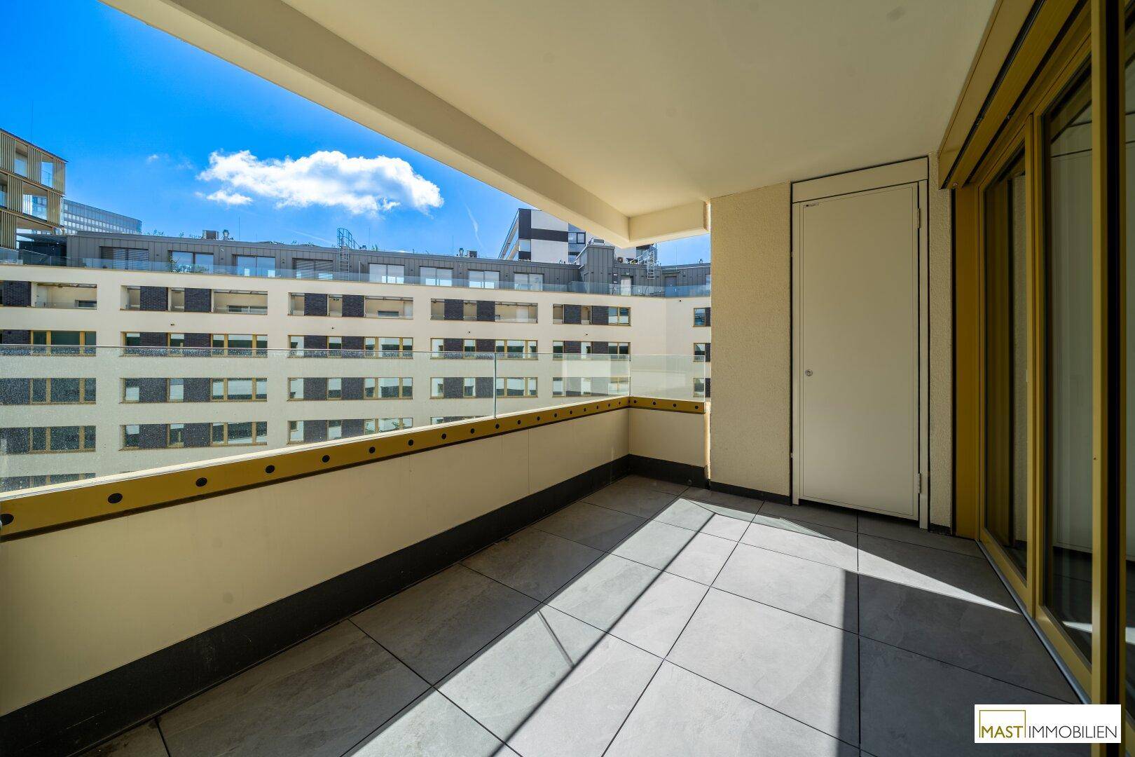 Geräumiger Balkon mit Fliesenboden und Blick auf die umliegenden Gebäude.