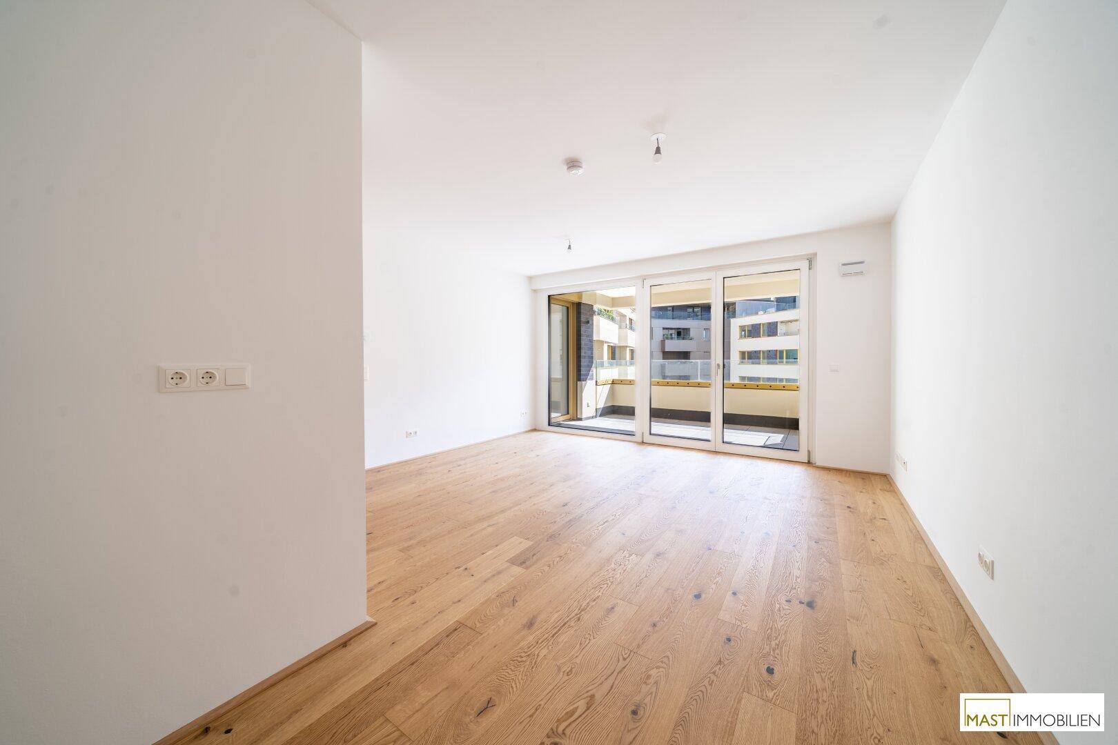 Geräumiges, unmöbliertes Zimmer mit Parkettboden und viel Tageslicht durch die Balkontür.
