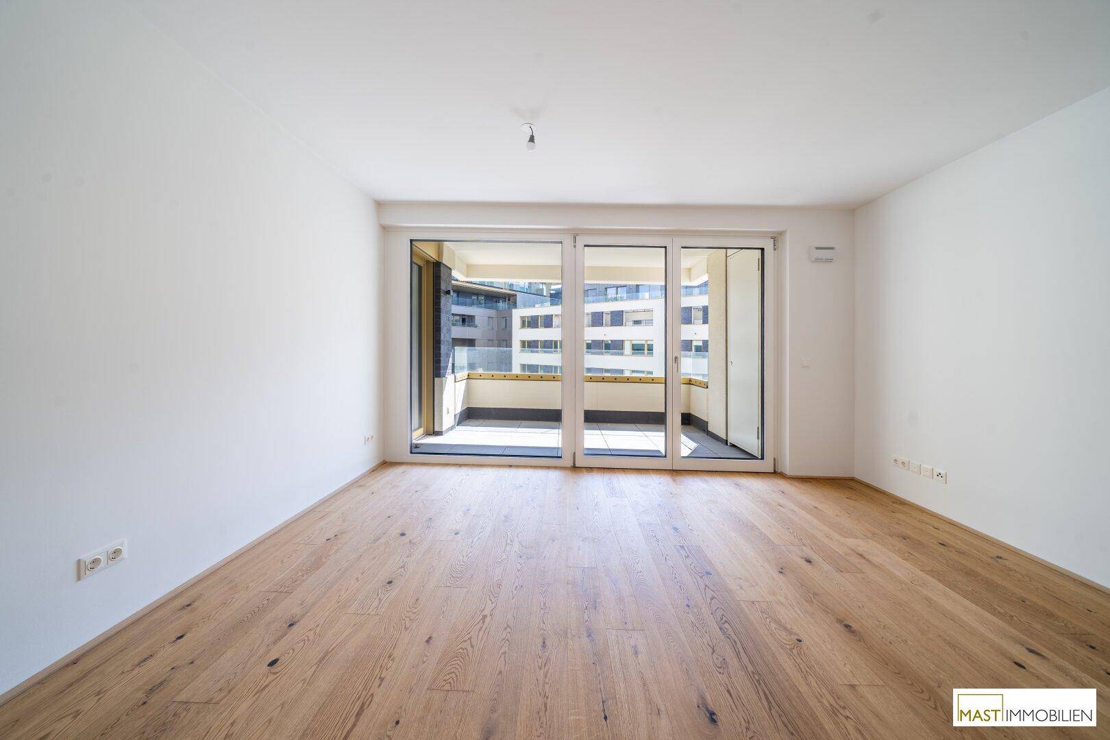 Lichtdurchfluteter Raum mit Holzboden und breiter Glasfront zum Außenbereich.