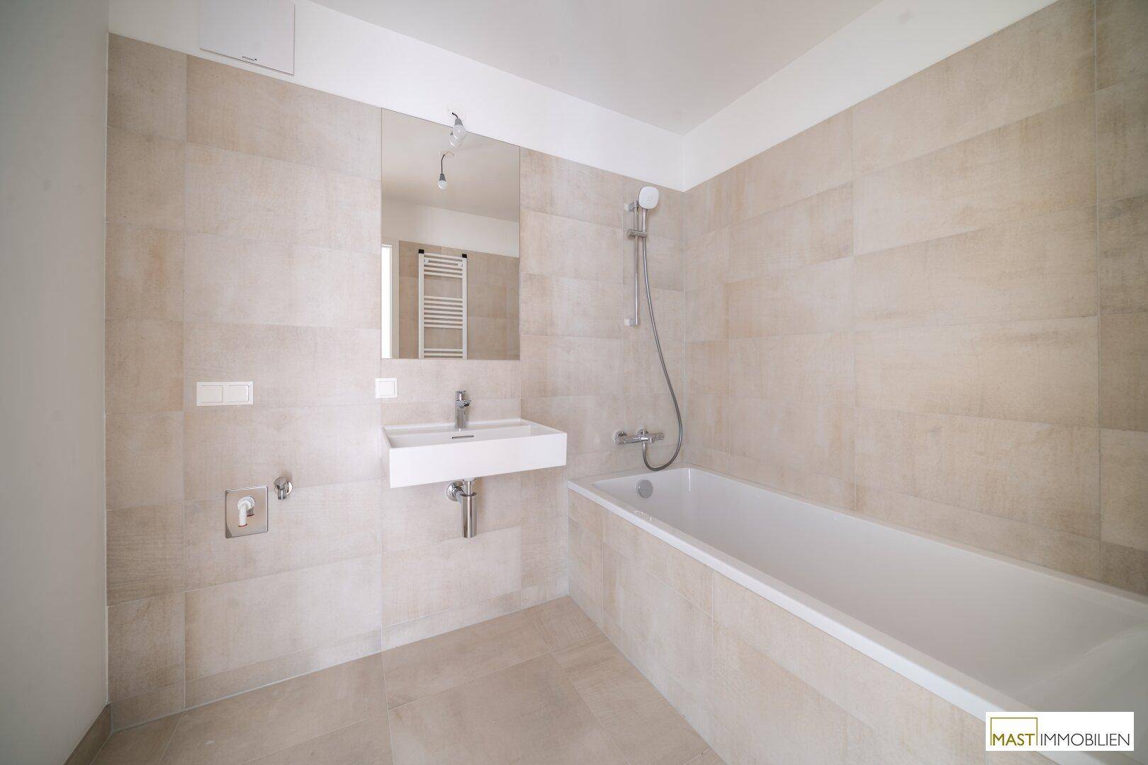 Modernes Badezimmer mit Badewanne, wandhängendem Waschbecken und großen Fliesen.