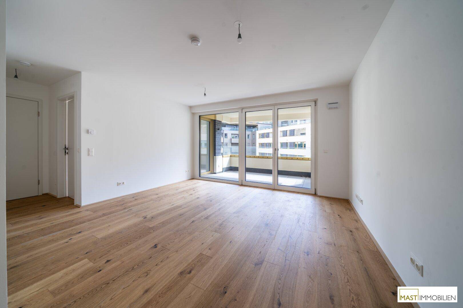 Heller, unmöblierter Wohnbereich mit Holzboden und Zugang zu einem Balkon.