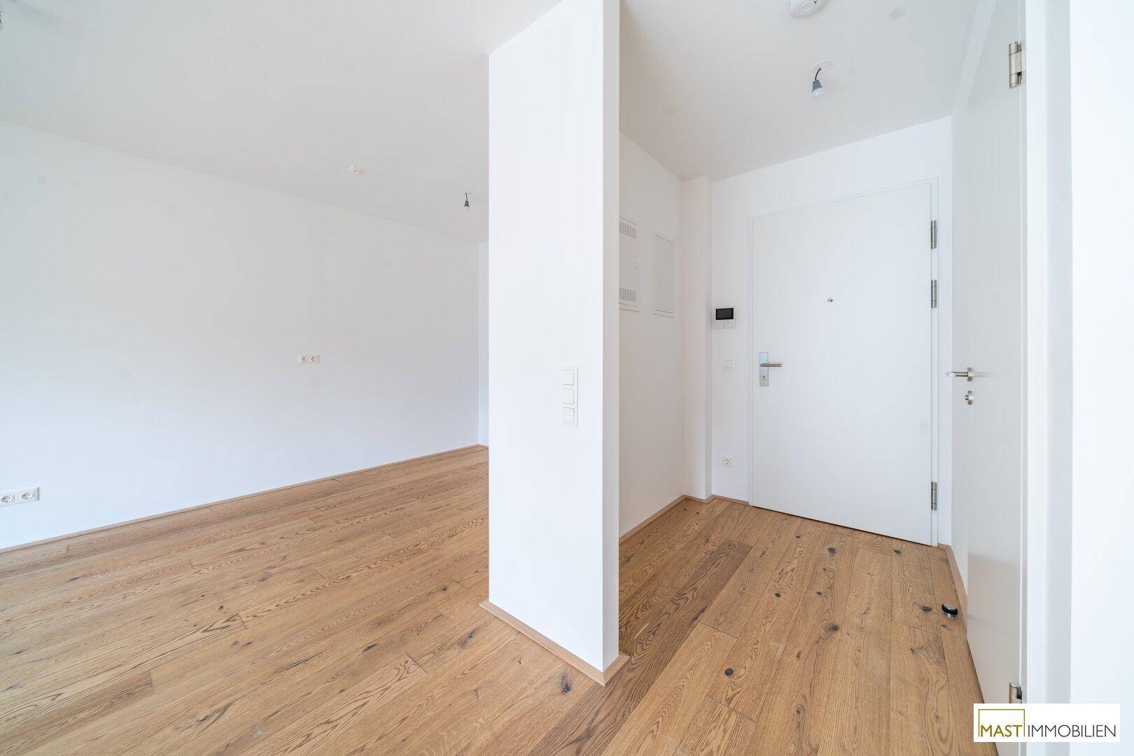 Heller Eingangsbereich mit Holzboden und weißer Eingangstür, führt in die Wohnräume.