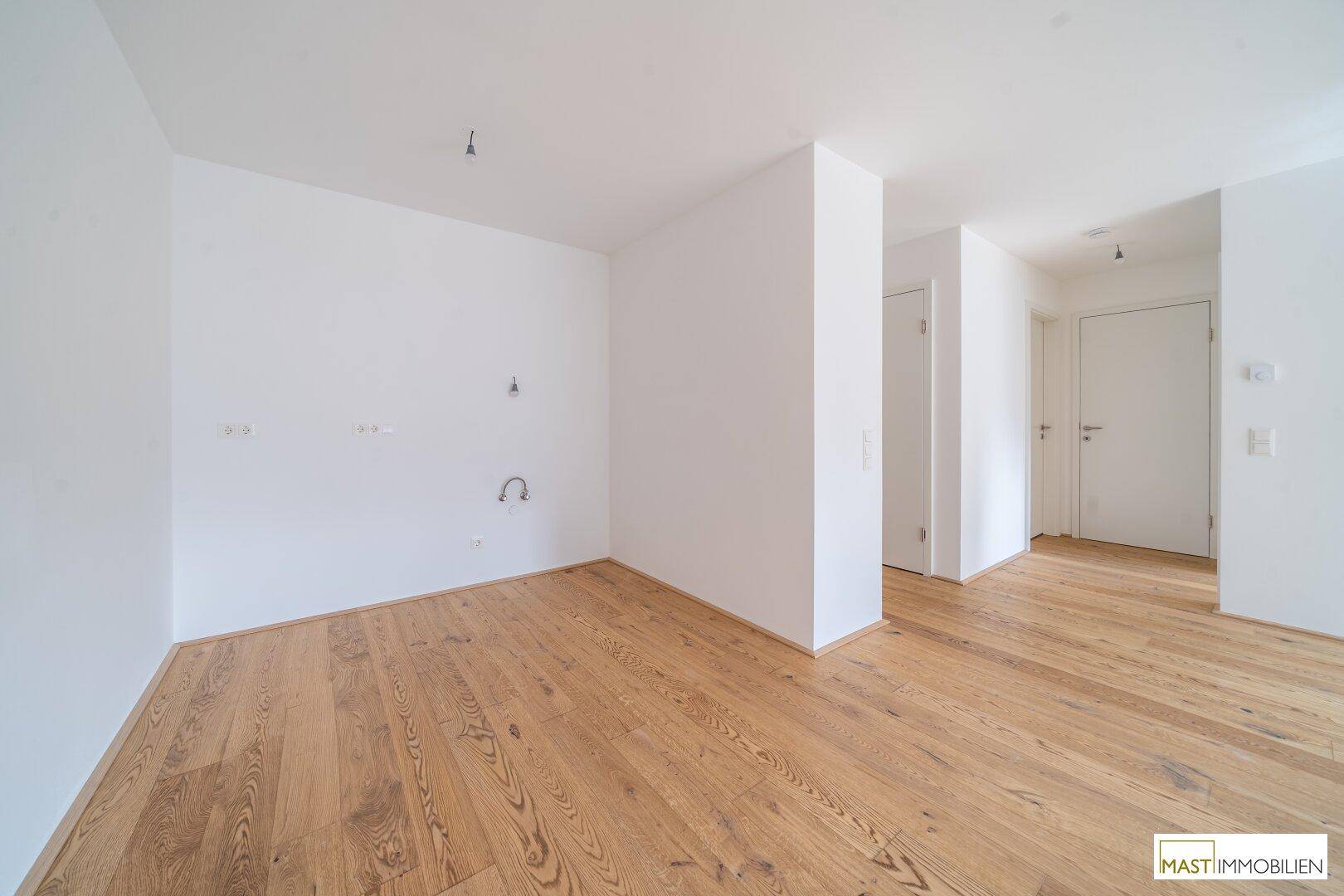 Leerer Küchenbereich mit Holzboden und Anschlüssen für eine Einbauküche, bereit zur Installation.