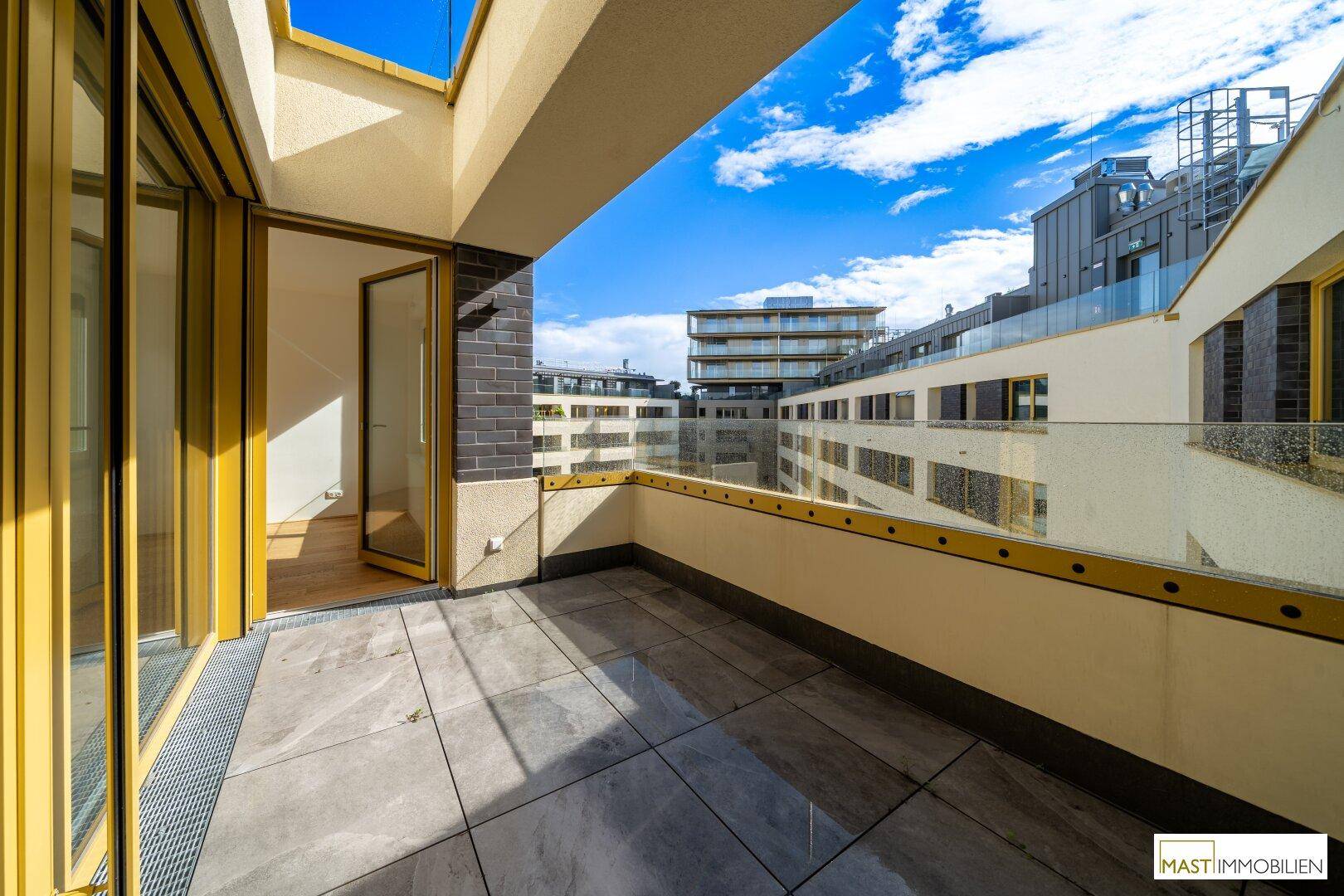 Geräumiger Balkon mit Fliesenboden und Glasgeländer, bietet einen Blick auf moderne Gebäude.