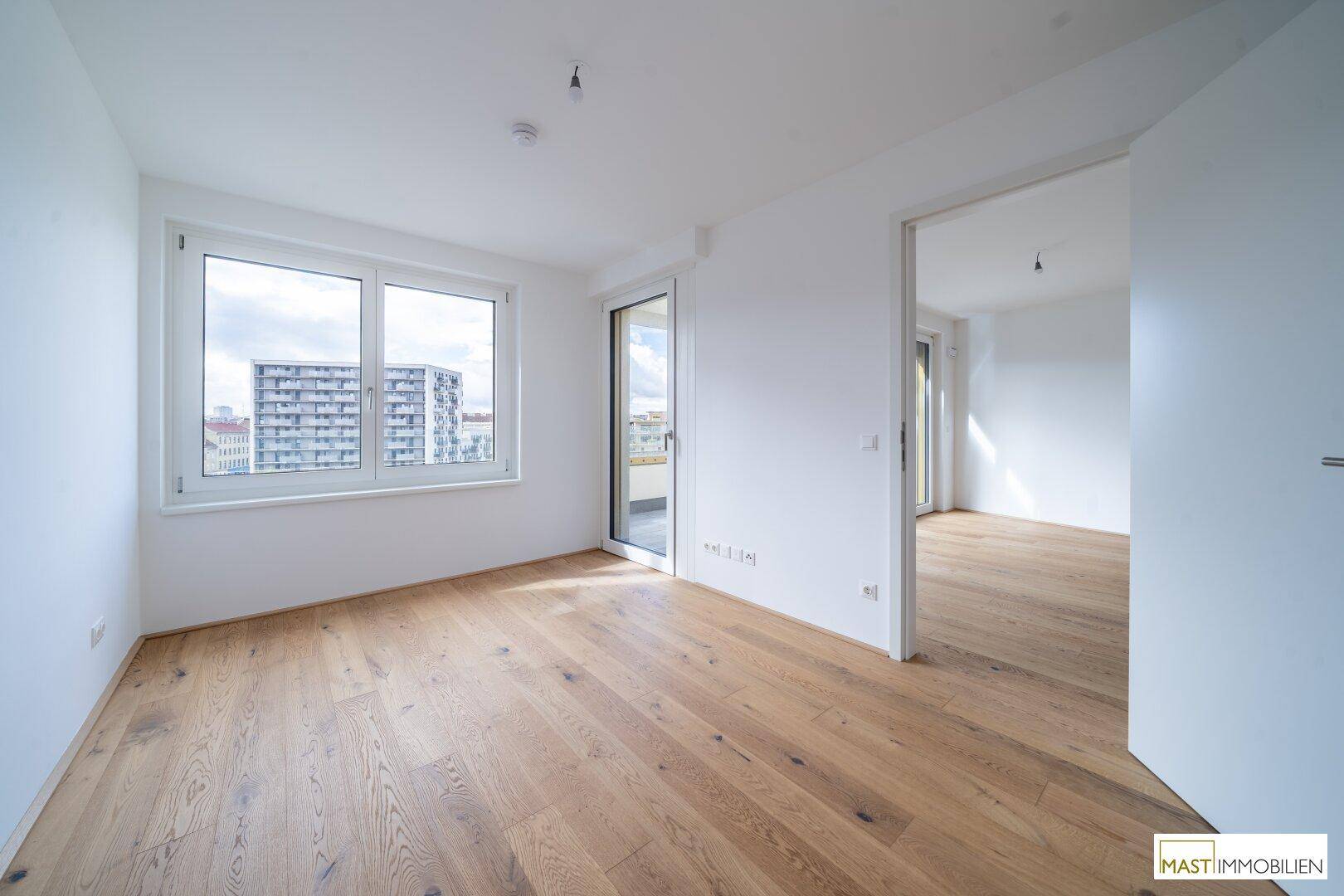 Helles Schlafzimmer mit Parkettboden und großen Fenstern mit Stadtblick.