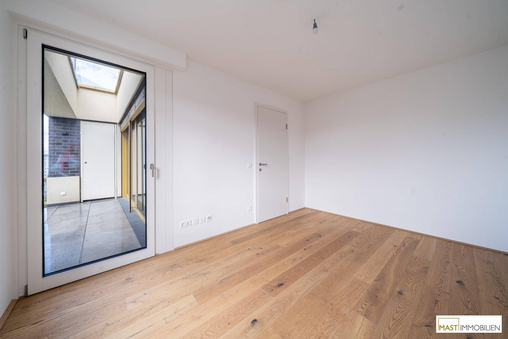 Geräumiges Schlafzimmer mit Holzboden und Zugang zu einem sonnigen Außenbereich.