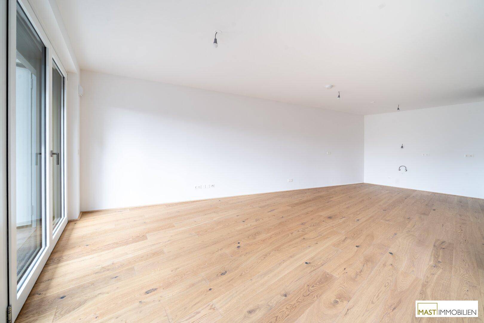 Offener Wohnbereich mit hellem Parkettboden und Zugang zum Balkon.