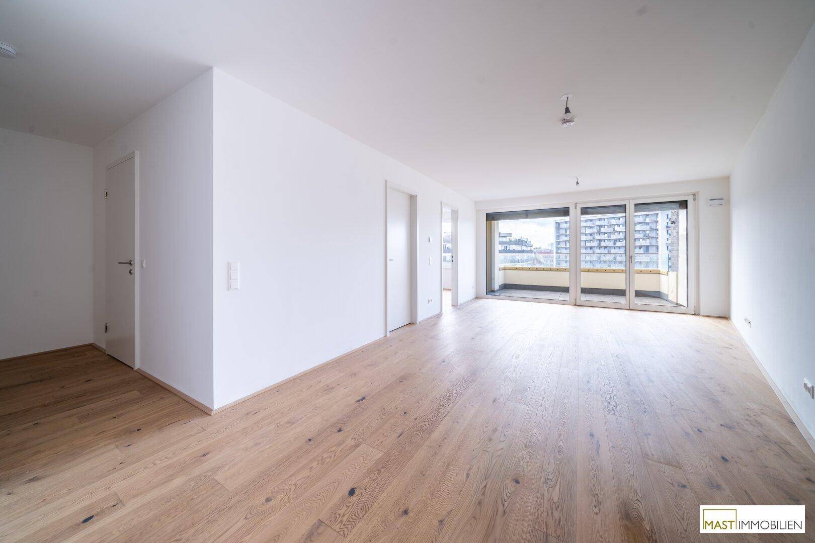 Geräumiges Wohnzimmer mit Holzboden und breiter Fensterfront zum Außenbereich.