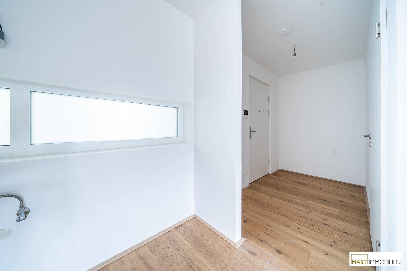 Heller Küchenbereich mit horizontalem Fenster und Anschlüssen für eine moderne Einbauküche.