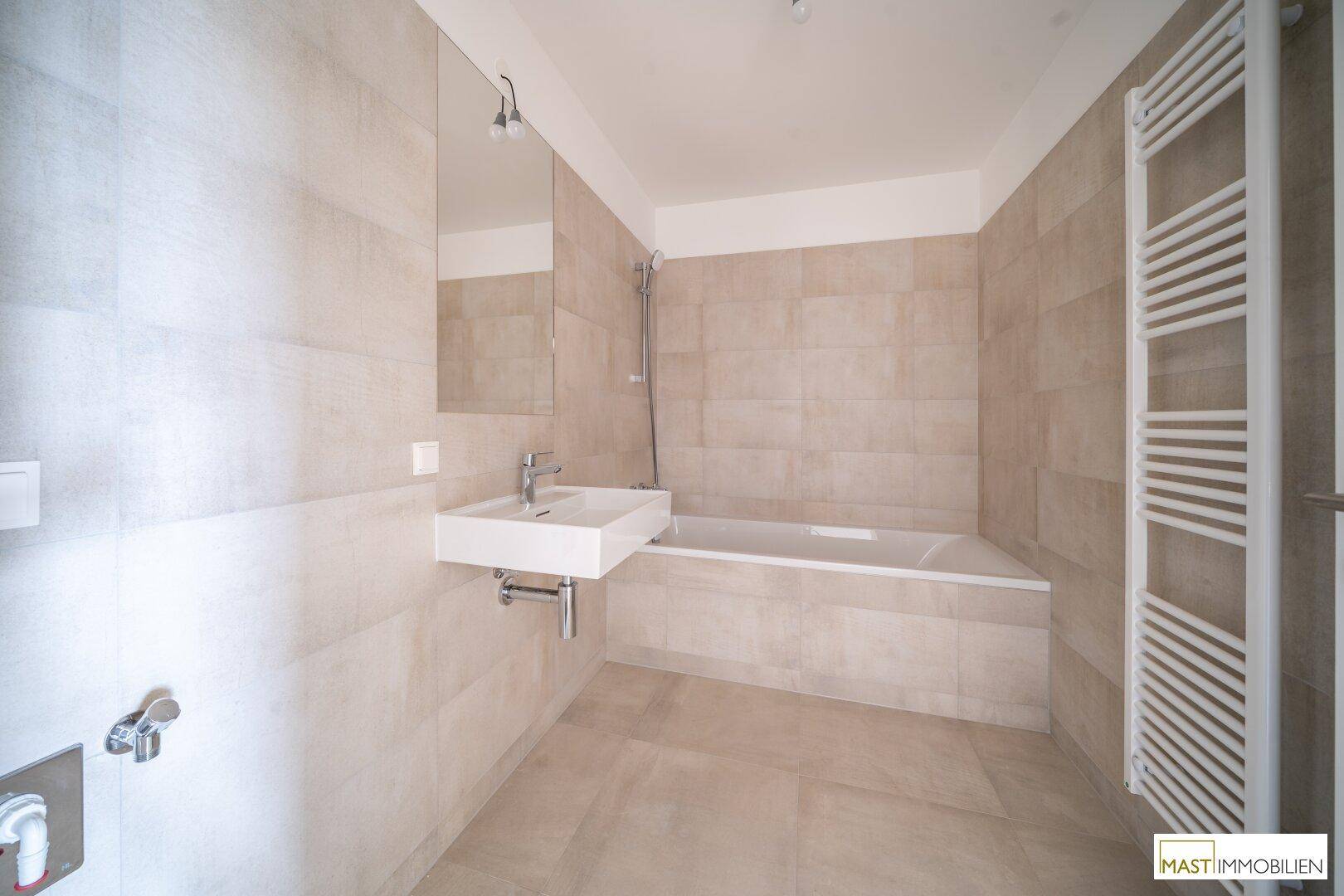 Modernes Badezimmer mit beigefarbenen Fliesen, Badewanne, Einzelwaschbecken und Handtuchheizkörper.
