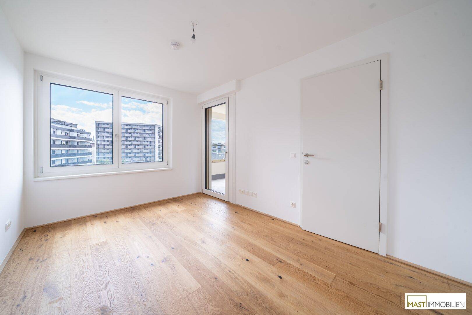 Helles Schlafzimmer mit Parkettboden, großen Fenstern und direktem Zugang zu einem Balkon.
