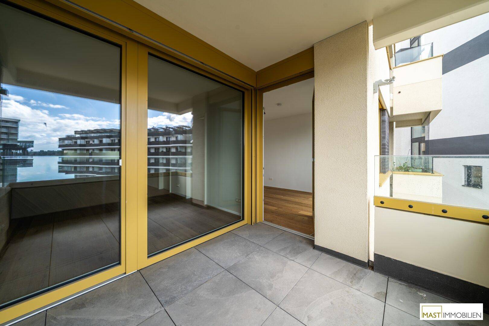 Heller Balkon mit Fliesenboden und großen Glasschiebetüren, die zum Innenbereich führen.