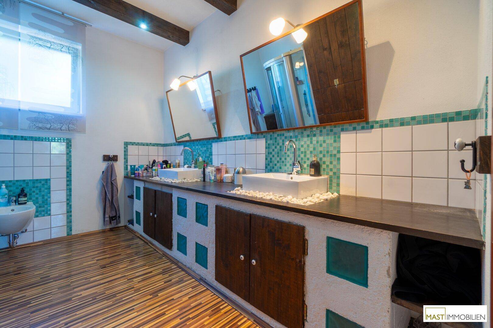 Rustikales Badezimmer mit Doppelwaschbecken, türkisen Mosaikfliesen und Holzbalken.