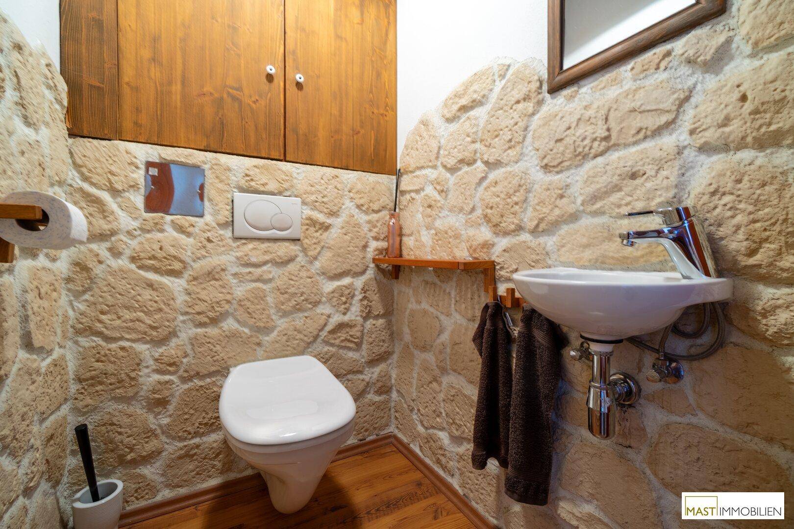 Rustikales Gäste-WC mit Natursteinwänden, Holzregalen und Wand-WC.
