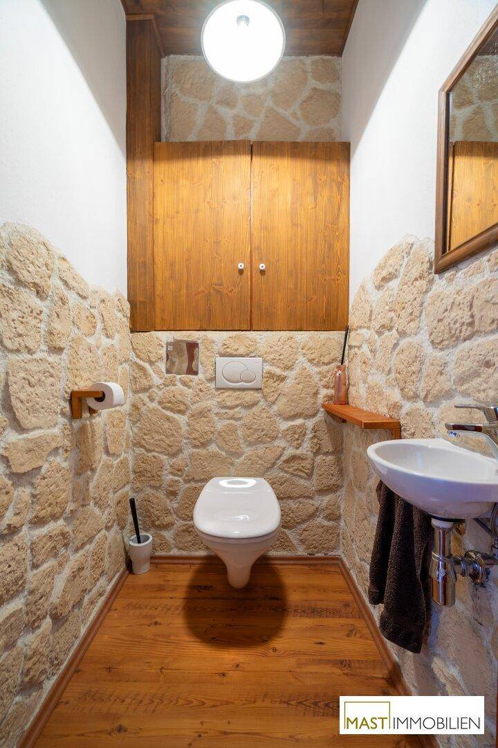 Kleines Gäste-WC mit Natursteinwänden, Holzdetails und schwebendem Waschbecken.