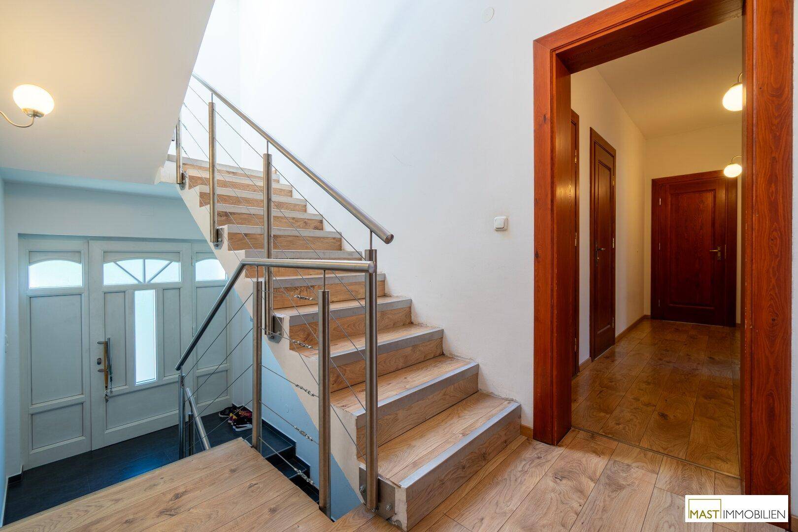 Eingangsbereich mit heller Holztreppe, Edelstahlgeländer und Holzboden.