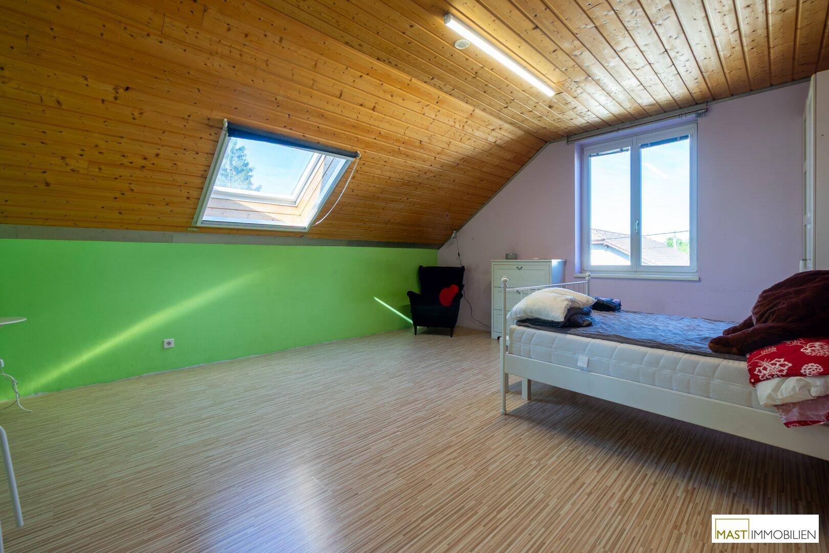 Farbiges Schlafzimmer im Dachgeschoss mit Holzdecke, Dachfenster und Laminatboden.